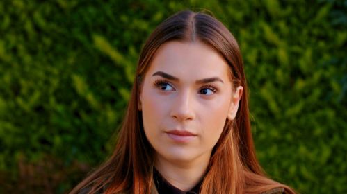 Sila spogląda w bok z lekkim zamyśleniem, jakby coś ją zaniepokoiło lub zastanowiło. Jej spojrzenie jest przenikliwe, a delikatny wyraz twarzy zdradza powagę chwili. Ciepłe światło podkreśla naturalne rysy i subtelny makijaż, tworząc spokojny, ale pełen emocji kadr. Serial „Miłość i nadzieja” można oglądać w TVP2 i na stronie vod.tvp.pl.