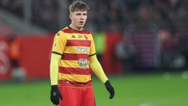 Oskar Pietuszewski (fot. Getty Images) Piłkarz Jagiellonii Białystok w żółto-czerwonej pasiasto poziomej koszulce meczowej z logo sponsorów, żółtych rękawach i czerwonych spodenkach, stojący na murawie stadionu podczas spotkania piłkarskiego. W tle widoczne rozmyte trybuny z kibicami