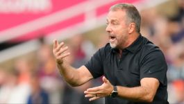 Hansi Flick (fot. Getty Images) Trener FC Barcelony Hansi Flick w czarnej koszulce polo gestykuluje podczas meczu, prawdopodobnie przekazując instrukcje zawodnikom. W tle widoczne są rozmyte sylwetki kibiców oraz fragment trybun z napisem 'BARCELONA' (fot. Getty Images)