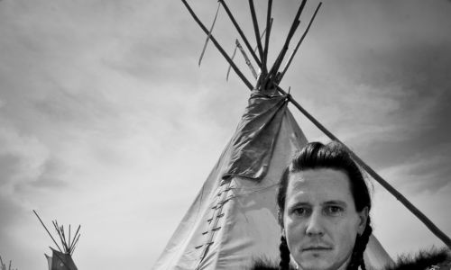 Dariusz Szybka w skórze, w tle tipi jego wioski. Odświętnie ubrani Indianie są głównie podczas ceremonii  i święta muzyki i tańca Pow-wow, które stanowi pomost między tradycją starą, kiedy jeszcze żyli na wolności, a współczesną, kiedy żyją w rezerwatach. Fot. Dariusz Zaród, archiwum prywatne DS