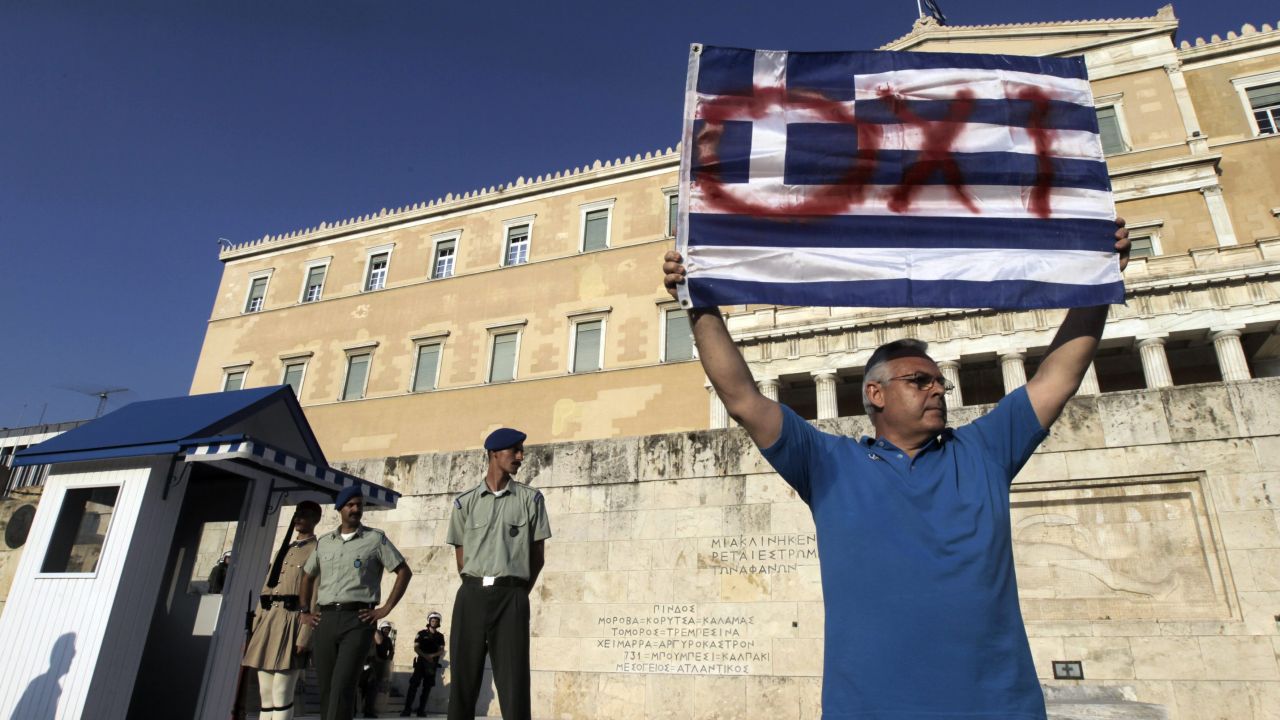 Mężczyzna trzyma grecką flagę z napisem NIE (fot. PAP/EPA/ORESTIS PANAGIOTOU)