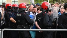 W centrum kadru widać szpaler funkcjonariuszy baskijskiej policji ERTZAINTZA w pełnym rynsztunku prewencyjnym — czarne mundury, czerwone hełmy i przezroczyste tarcze tworzą wyraźną linię oddzielającą ich od tłumu. Za nimi gęsto stłoczona grupa kibiców, z których wielu ma na sobie klubowe barwy i szaliki, co sugeruje atmosferę przedmeczowego napięcia. Twarze w tłumie są skupione, część osób patrzy w stronę funkcjonariuszy, część w kierunku obiektywu, co potęguje wrażenie niepewności (fot. Getty Images)