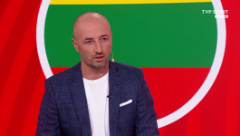 Zdjęcie przedstawia Łukasza Trałkę, byłego reprezentanta Polski, siedzącego w studiu telewizyjnym TVP Sport na tle grafiki w kolorach flagi Litwy (żółty, zielony, czerwony). Trałka, ubrany w niebieską marynarkę i białą koszulkę, komentuje w programie "Odliczanie do mundialu" potencjalne powołania zawodników kadry U21 do seniorskiej reprezentacji, stwierdzając, że "to nie są zawodnicy na teraz", mimo pochwał dla obrony młodzieżówki (fot. TVP)