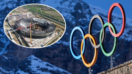 Koła olimpijskie w Cortinie d'Ampezzo i nieskończona wciąż PalaItalia Santa Giulia (fot. Getty Images) Grafika przedstawiająca przygotowania do zimowych igrzysk olimpijskich w Mediolanie i Cortinie d'Ampezzo. Na pierwszym planie widoczne są kolorowe pierścienie olimpijskie na tle ośnieżonych gór. W lewym górnym rogu znajduje się wstawka z budową jednej z aren – nowoczesnego stadionu otoczonego dźwigami. Obraz symbolizuje podział olimpijskiego obszaru na cztery klastry, rozmieszczenie sześciu wiosek olimpijskich oraz wyzwania logistyczne związane z organizacją igrzysk na rozległym terenie