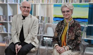 Jerzy Antczak i Jadwiga Barańska siedzą obok siebie na przezroczystych krzesłach i uśmiechają się do obiektywu.