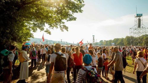 Duży tłum ludzi na pielgrzymce na świeżym powietrzu w słoneczny dzień.