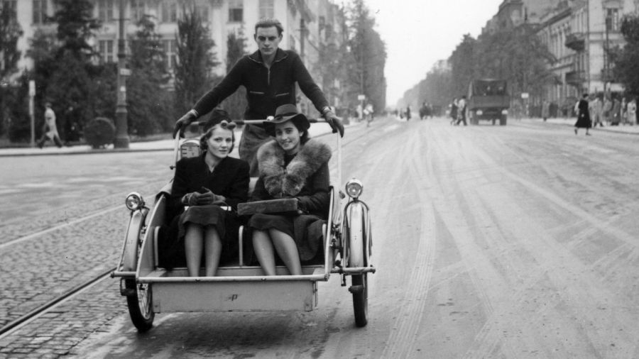Okupacja Warszawy, między 1940 a 1944 rokiem. Kobiety w rikszy jadące przez pl. Trzech Krzyży. W tle z lewej gmach X Gimnazjum i Liceum im. Królowej Jadwigi oraz zabudowa Al. Ujazdowskich. Fot. NAC/ Mieczysław Bilażewski-Bil, Wydawnictwo Prasowe Kraków-Warszawa, sygnatura: 2-7982