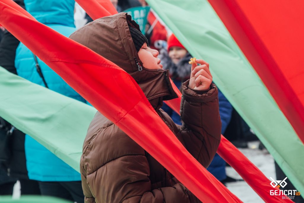 Дзіцё сярод чырвона-зялёных сцягоў на «Прыгожым забегу» у Жодзіна. 8 сакавіка 2021. (Фота: ТК / Белсат)
